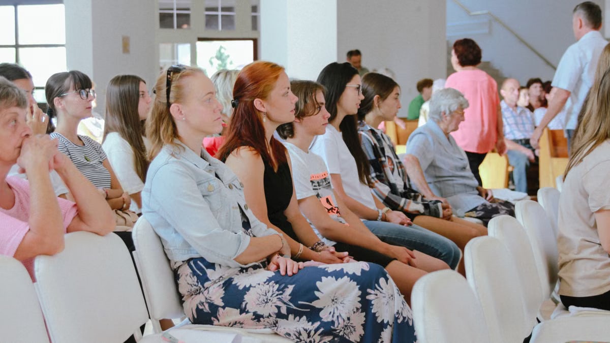 A diverse group of people sitting attentively during an indoor meeting or event, captured in a spacious room.
